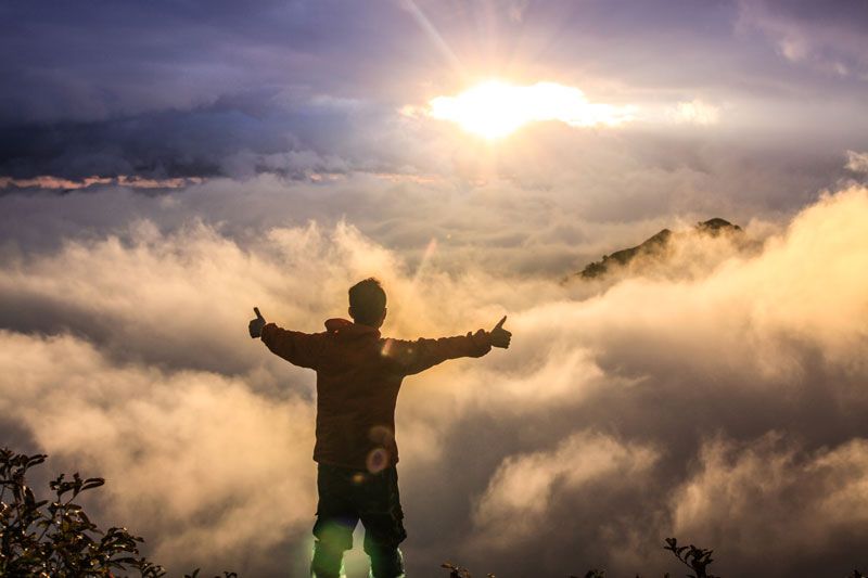 man with thumbs up looking at sunrise through cloudy skies